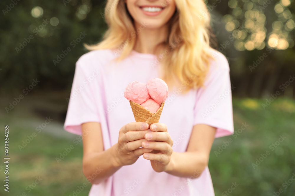Happy young woman with delicious ice cream in waffle cone outdoors, closeup
