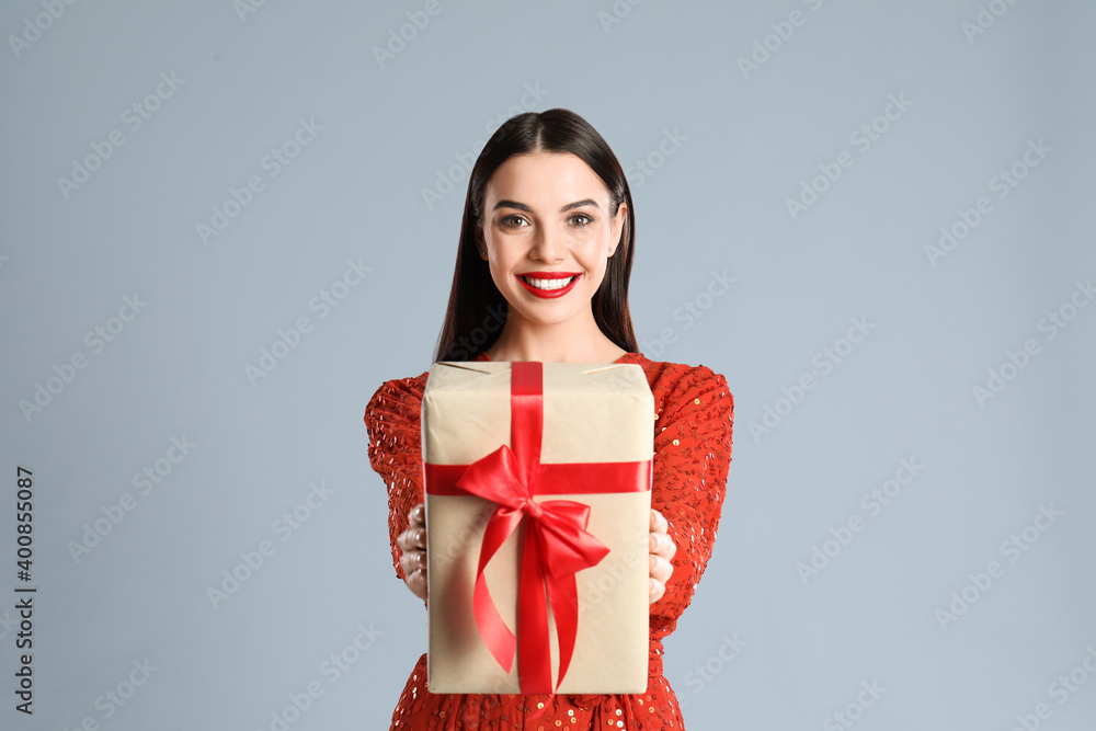 Fototapeta premium Woman in red dress holding Christmas gift on grey background