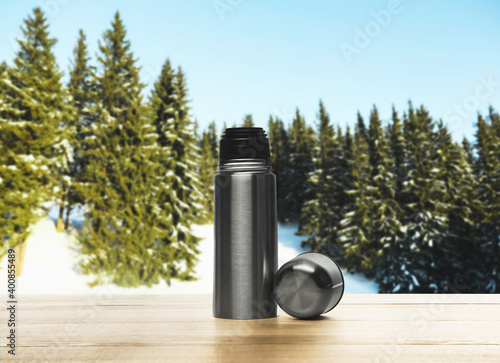 Thermos bottle on wooden table in snowy forest