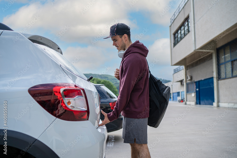 Mid adult man opening car trunk while standing at parking lot Mid adult man opening car trunk while standing at parking lot