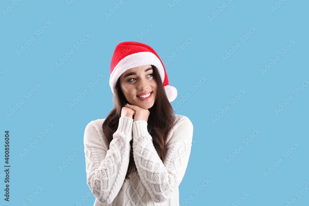 Beautiful woman wearing Santa Claus hat on light blue background Beautiful woman wearing Santa Claus hat on light blue background