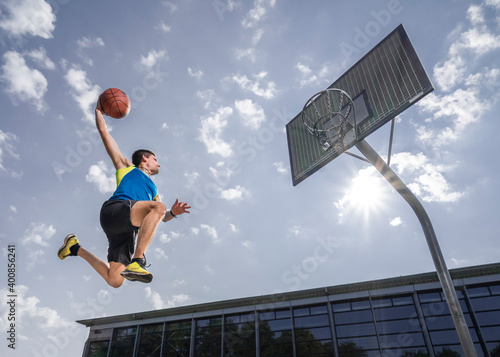 Young male athlete dunking ball in hoop while playing basketball on sunny day photo