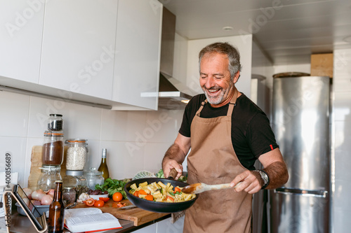 Smiling mature man preparing pasta while standing in kitchen at home