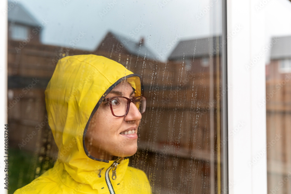 Woman looking through window while standing at home during rainy season Woman looking through window while standing at home during rainy season