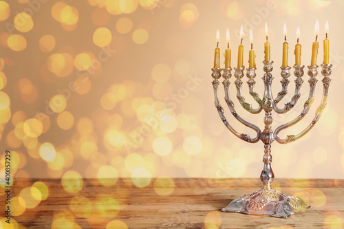 Silver menorah with burning candles on wooden table against beige background, space for text. Hanukkah celebration