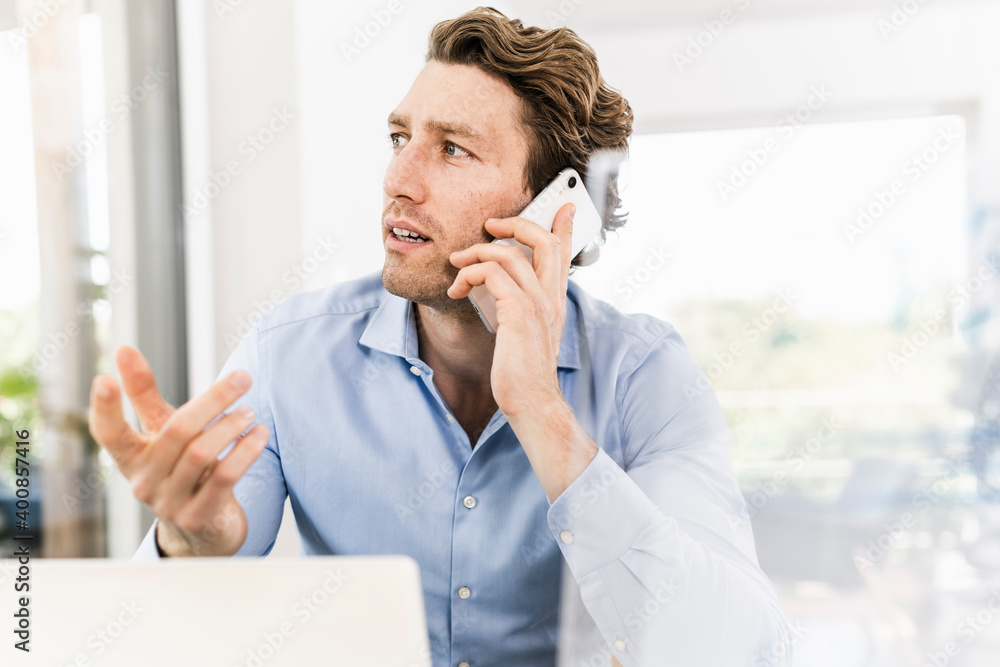 Mid adult man talking on smart phone looking away while sitting in office Mid adult man talking on smart phone looking away while sitting in office