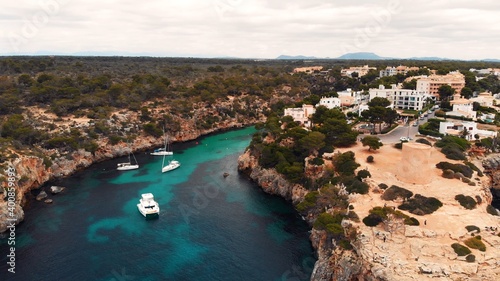 Floating boats in crystal clear Mediterranean sea with coral reef and cliffs, Mallorca, Cala pi, Cala Satanyi, Aerial. High quality photo