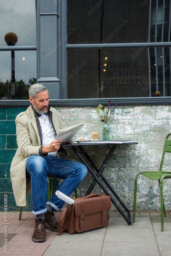 Mature businessman reading newspaper while sitting at sidewalk cafe Mature businessman reading newspaper while sitting at sidewalk cafe