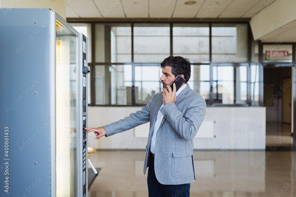 Professor talking on mobile phone while using vending machine in cafeteria at university Professor talking on mobile phone while using vending machine in cafeteria at university