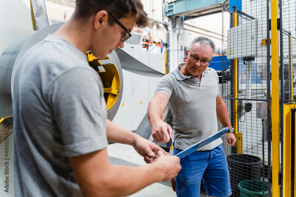 Male coworkers brainstorming while standing against machinery in industry Male coworkers brainstorming while standing against machinery in industry