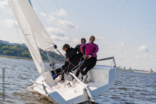 A fast, sporty, single-masted yacht with three athletes on board sails with a fair wind on a beautiful river