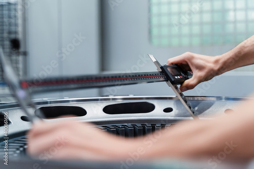 Mature male engineer's hands measuring machine with measurement tool at illuminated factory