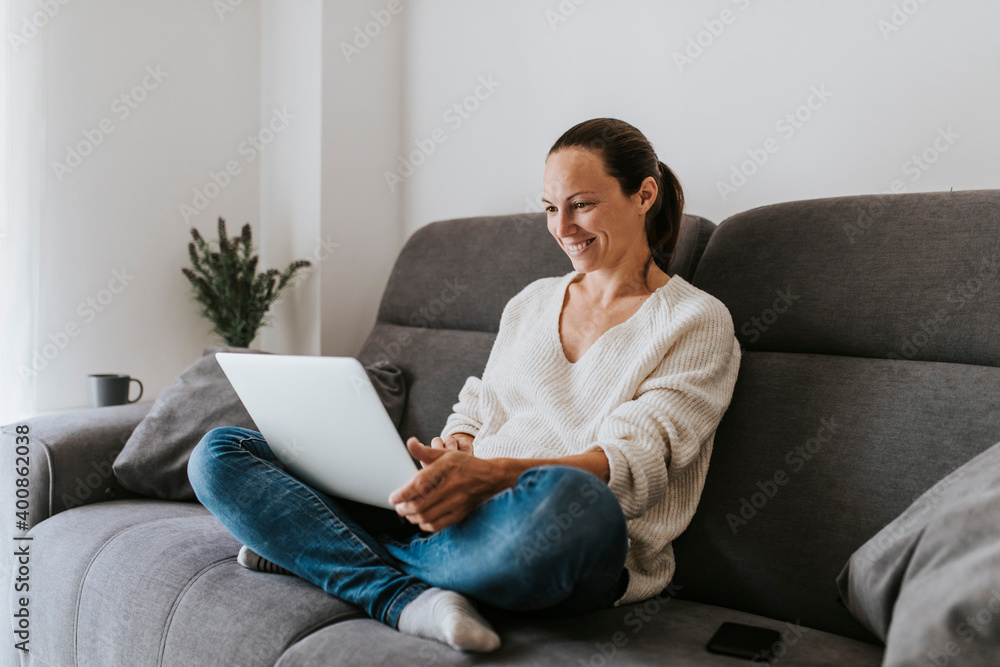 Smiling woman sitting cross-legged using laptop on sofa in living room Smiling woman sitting cross-legged using laptop on sofa in living room