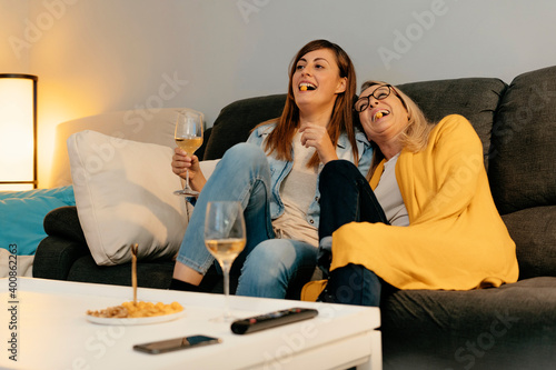 Mother and daughter laughing while eating snacks in living room at home photo