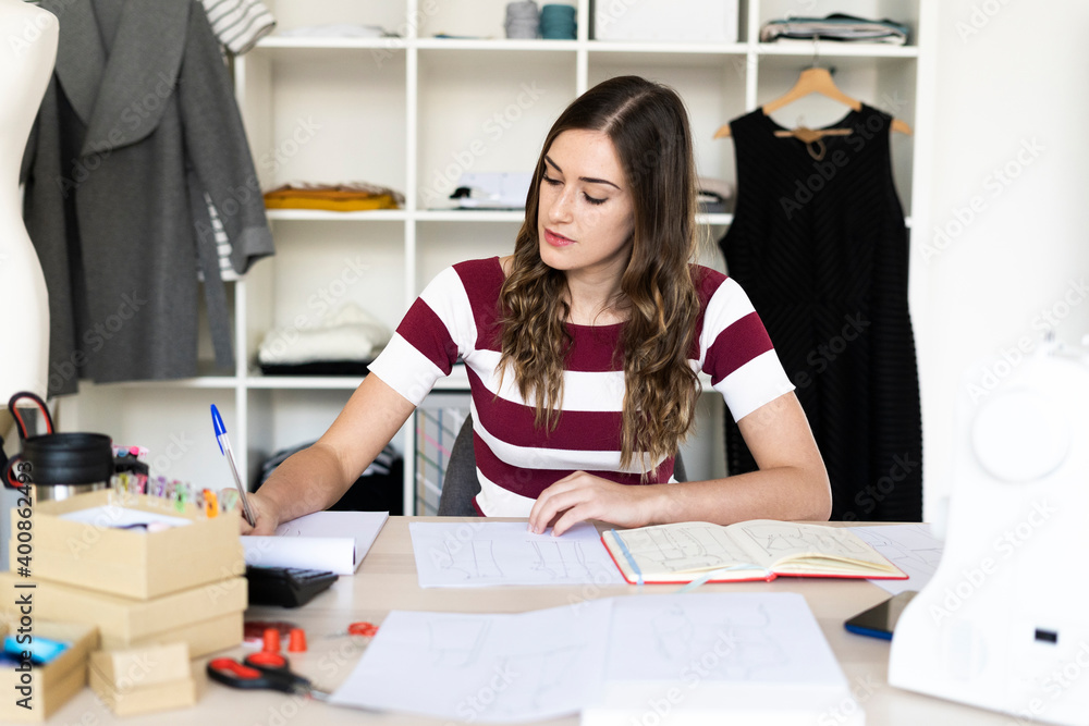 Female fashion designer writing in book while sitting at studio Female fashion designer writing in book while sitting at studio