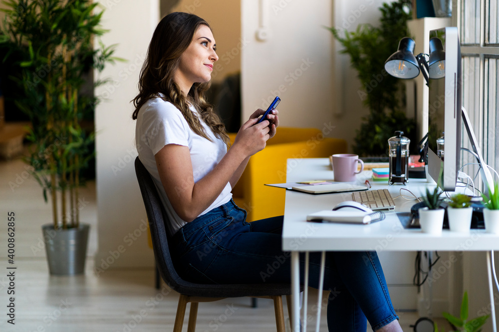 Thoughtful businesswoman holding smart phone while sitting in office Thoughtful businesswoman holding smart phone while sitting in office