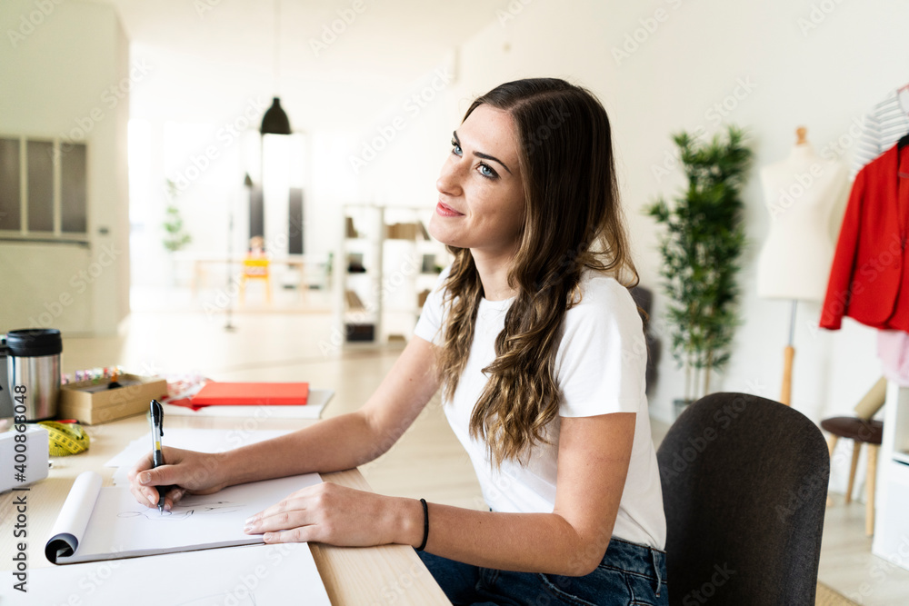 Thoughtful female creative designer drawing in book while sitting at studio Thoughtful female creative designer drawing in book while sitting at studio