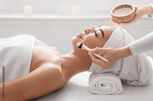Skin Care. Cosmetologist applying moisturising clay mask on young asian woman face