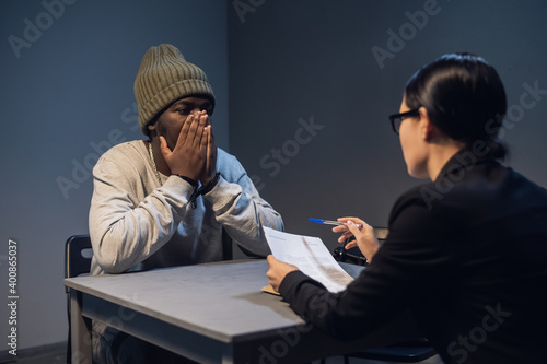 A young girl lawyer consults her client at the police station, a black guy in a cap and handcuffs