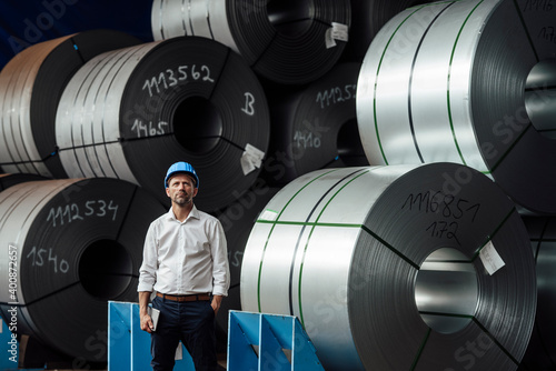 Male owner with hand in pocket standing against steel rolls in industry photo