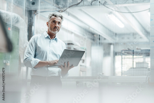 Contemplating male engineer with laptop looking away while standing in industry photo