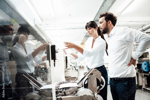 Male and female engineers looking at paper while investigating machinery in manufacturing industry