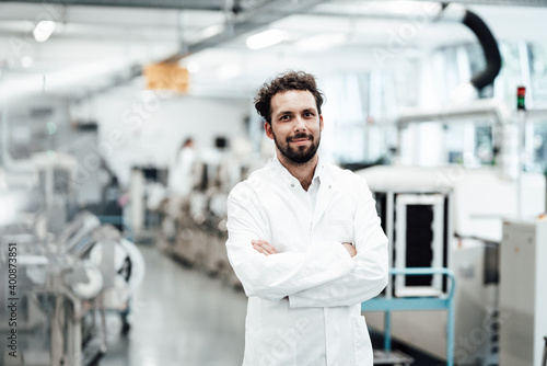 Confident male scientist in white lab coat while standing with arms crossed at bright laboratory photo