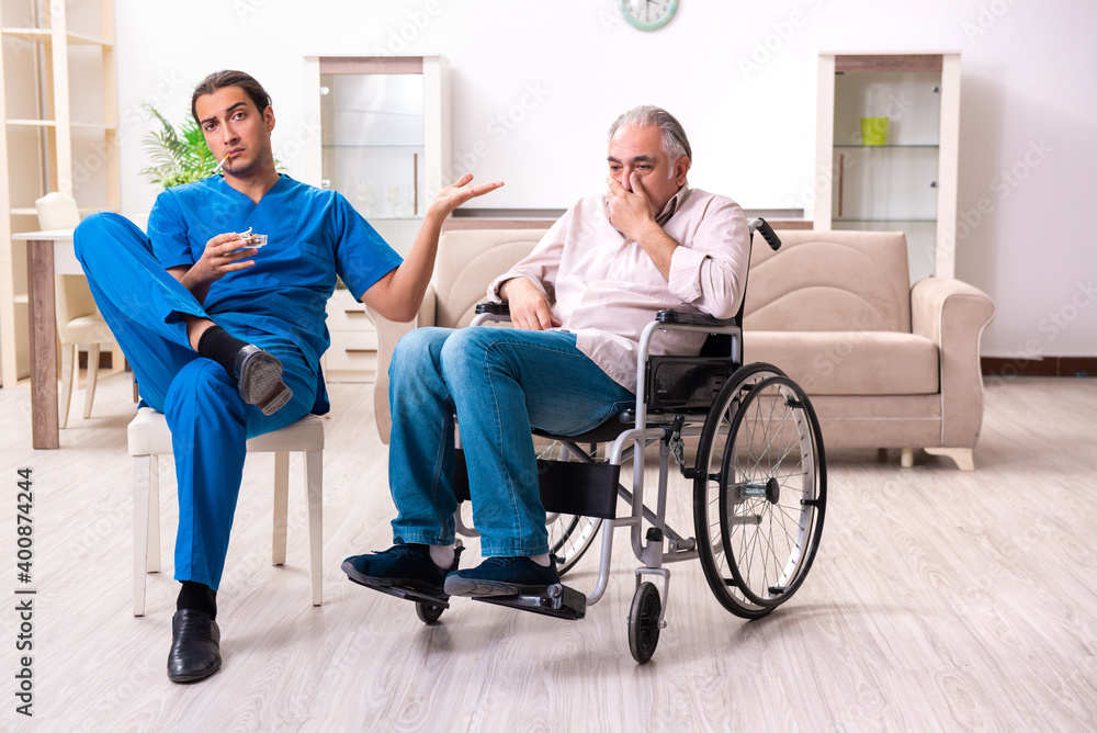 Old man in wheel-chair and young bad caregiver indoors Old man in wheel-chair and young bad caregiver indoors