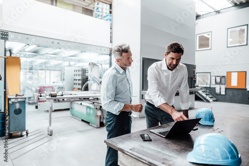 Male engineer pointing while discussing over laptop with colleague in manufacturing industry