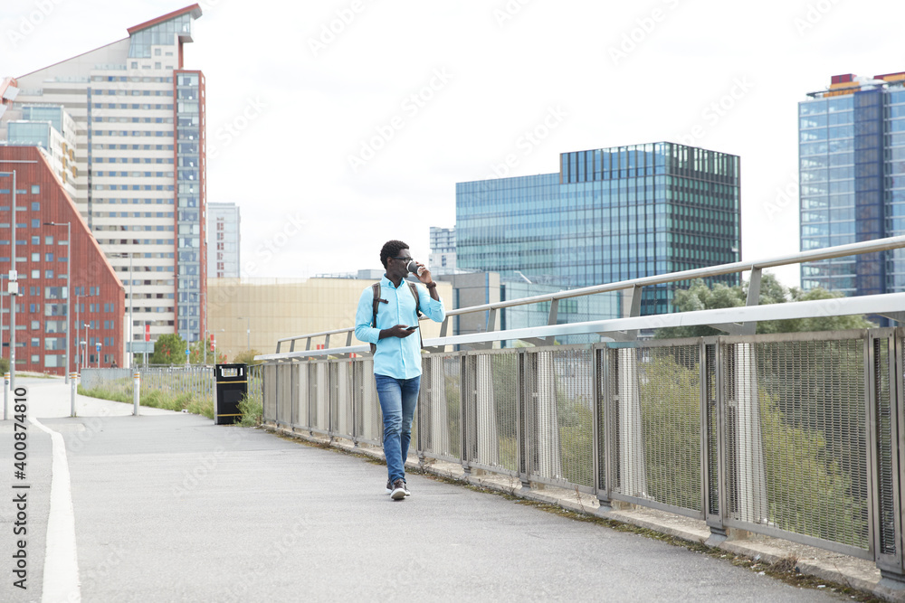 Mature man drinking coffee while holding smart phone walking on footpath in city Mature man drinking coffee while holding smart phone walking on footpath in city