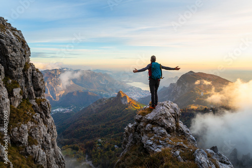 Pensive hiker with arms outstretched standing on mountain during sunrise at Bergamasque Alps, Italy