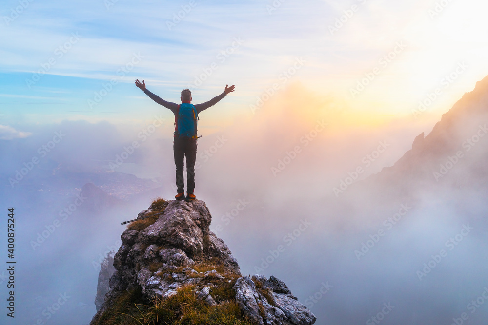 Pensive male hiker with arms outstretched standing on mountain peak during sunrise at Bergamasque Alps, Italy Pensive male hiker with arms outstretched standing on mountain peak during sunrise at Bergamasque Alps, Italy