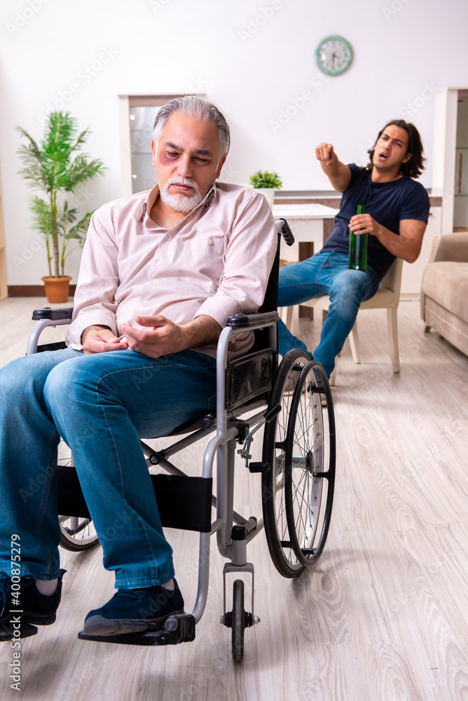 Old man in wheel-chair and young bad caregiver indoors Old man in wheel-chair and young bad caregiver indoors