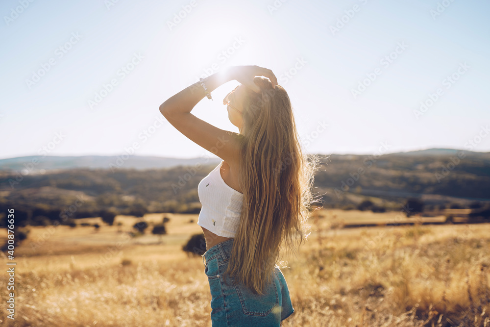 Young woman with hand in hair standing on field against sky during sunny day Young woman with hand in hair standing on field against sky during sunny day