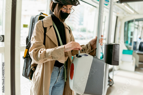 Woman wearing face mask and cycling helmet putting ticket in ticket validation machine while standing in tram