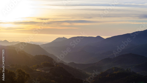 Mountain forest peak landscape on a sunrise morning with some tiny mist fog in the valleys on a yellow sunny sky sunrise © jordieasy