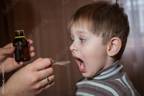 Mom gives her son cough medicine.