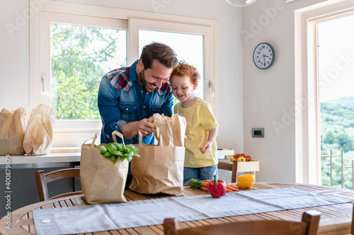 Smiling man showing groceries to son in kitchen at home photo