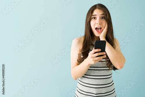 Beautiful woman touching her hace looking happy and shocked with her cellphone