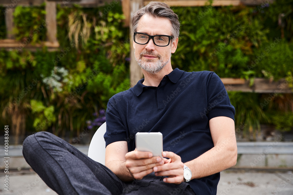 Thoughtful mature man holding smart phone while sitting at yard Thoughtful mature man holding smart phone while sitting at yard