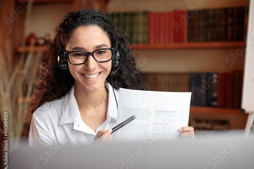 Woman in glasses sitting at desk, having videocall on laptop photo