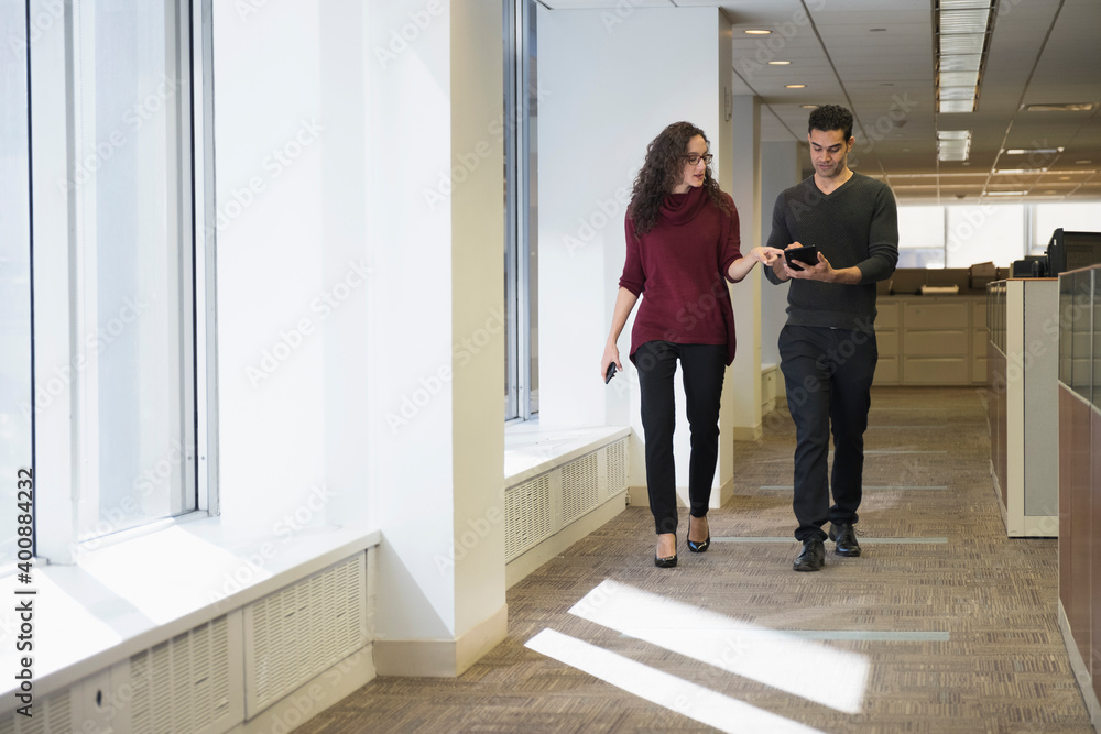 Young people walking side by side in corridor with digital tablet Young people walking side by side in corridor with digital tablet