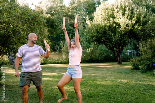 Father looking at daughter with hand raised while playing molkky in yard photo