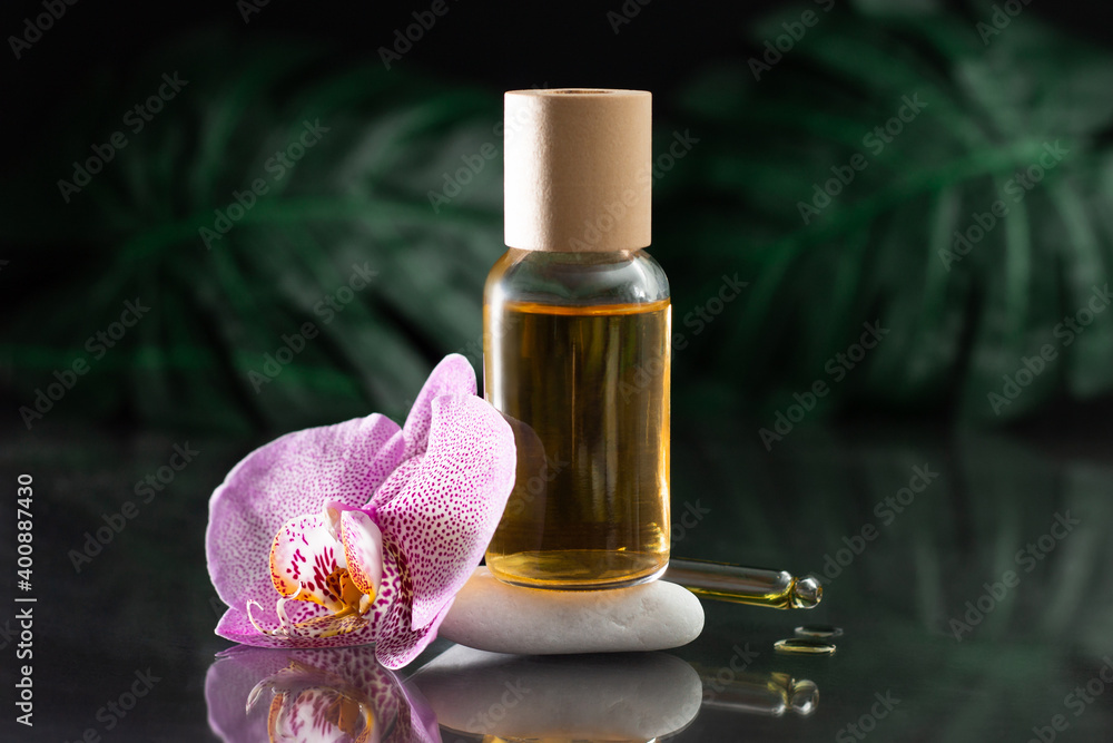 Lilac orchid and clear glass bottle of yellow oil standing on white stone with dropper on black reflective surface Lilac orchid and clear glass bottle of yellow oil standing on white stone with dropper on black reflective surface