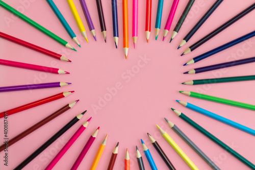 Heart laid out with sharpened multi-colored pencils on a pink background, flat lay, copy space.