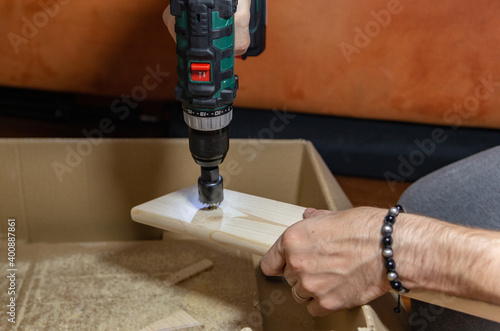 a man using an electric drill at home to drill a hole in a wooden board. Do it yourself. 