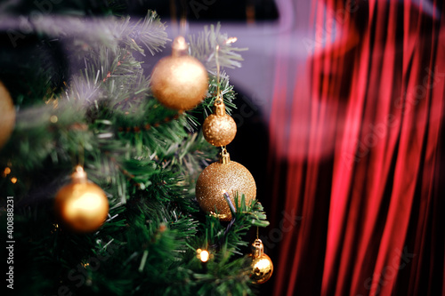 Magical green pine branches with traditional, shiny, golden christmas ornaments and a red blurred curtain in the background. Close-up shot of an X-mas tree for a wallpaper, poster, holiday card.