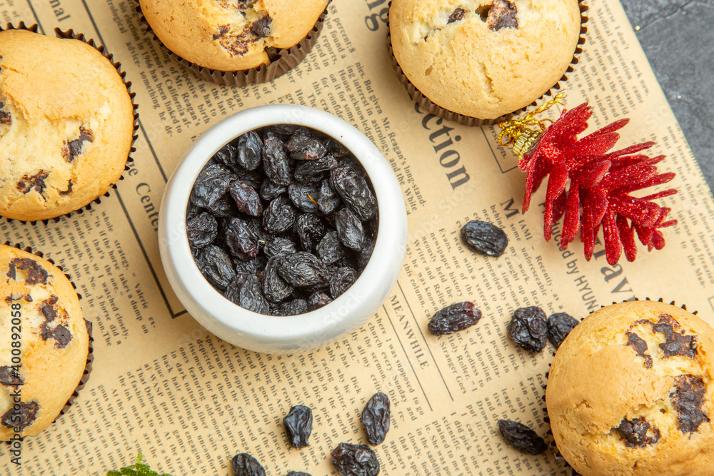 Tasty small cupcakes black raisin and accessories on newspaper on dark isolated background Tasty small cupcakes black raisin and accessories on newspaper on dark isolated background