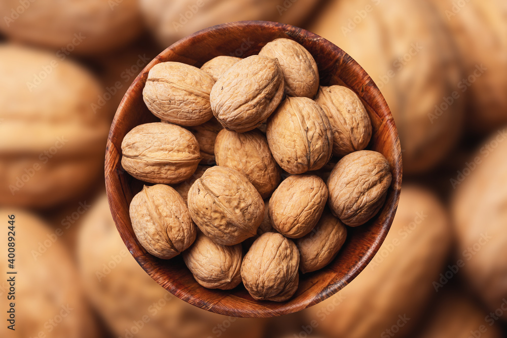 Walnuts background. Walnuts in wooden bowl. Whole nuts in shells in round container with empty copy space for graphic design text. Healthy food ingredient texture. Walnuts background. Walnuts in wooden bowl. Whole nuts in shells in round container with empty copy space for graphic design text. Healthy food ingredient texture.