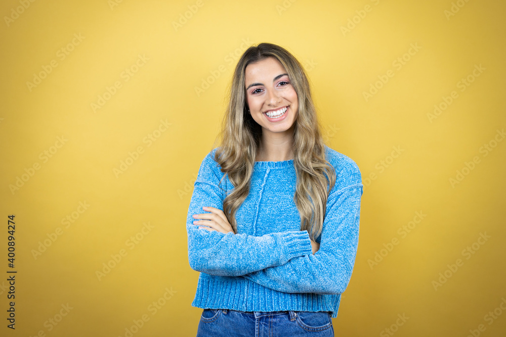 Pretty blonde woman with long hair standing over yellow background with a confident smile showing teeth with arms crossed Pretty blonde woman with long hair standing over yellow background with a confident smile showing teeth with arms crossed